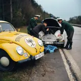 Das Titelbild des neuen ADAC Oldtimer-Ratgebers zeigt einen Gelben Engel, der havarierten Polizisten in den 1960er Jahren hilft